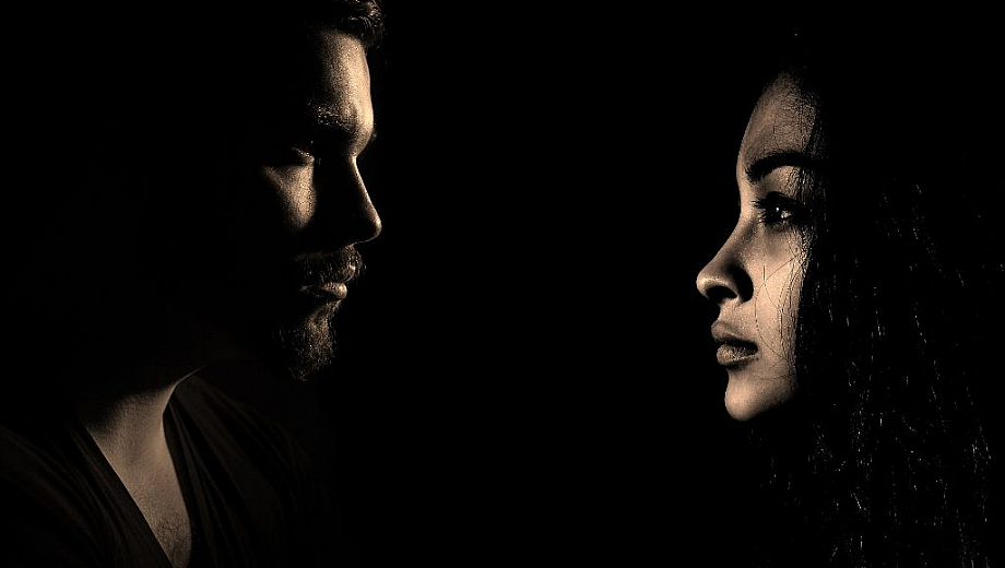 Ein Mann und eine Frau schauen sich gegenseitig an. Ihre Gesichter sind ausdruckslos. Um sie herum ist alles schwarz.