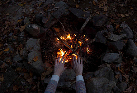 Zwei Hände wärmen sich an einem Lagerfeuer.