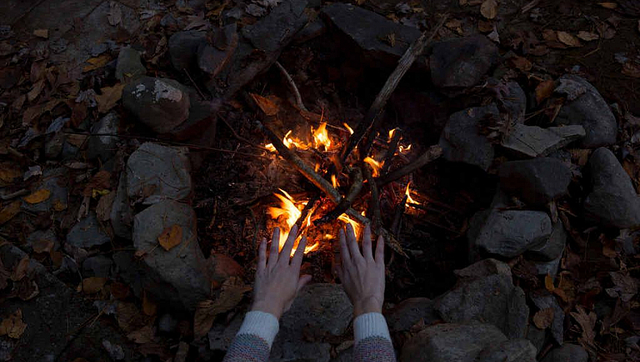 Zwei Hände wärmen sich an einem Lagerfeuer.