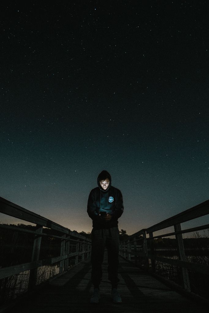 Bei dunkler Nacht steht ein Mann auf einer Brücke und guckt in das hell erleuchtete Disply seines Smartphones.