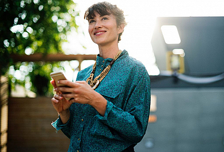 Eine Frau hält ein Smartphone in den Händen und guckt lächelnd in die Luft.