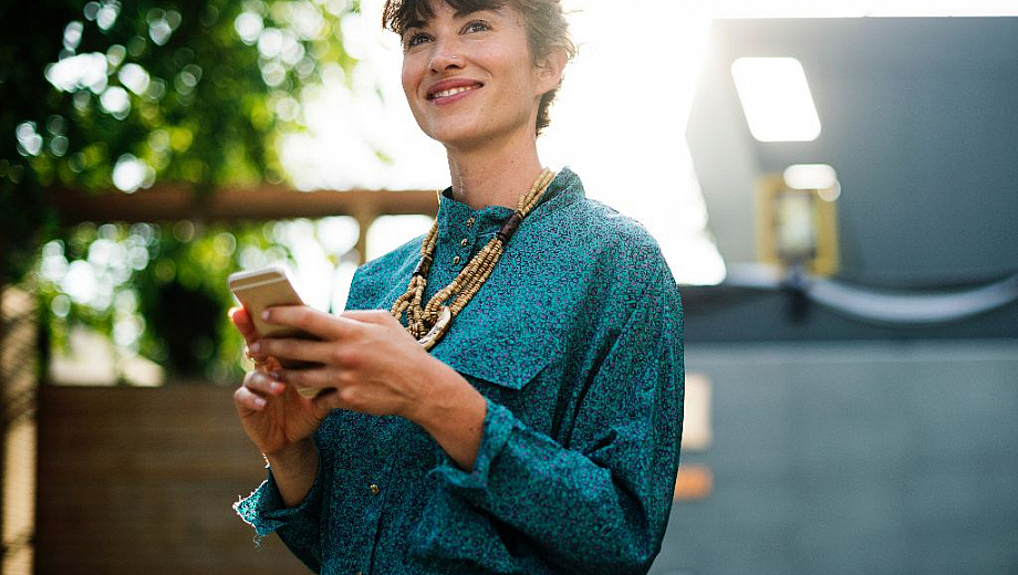 Eine Frau hält ein Smartphone in den Händen und guckt lächelnd in die Luft.