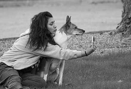 Eine Frau sitzt im Park und macht ein Selfie von sich und ihrem Hund.