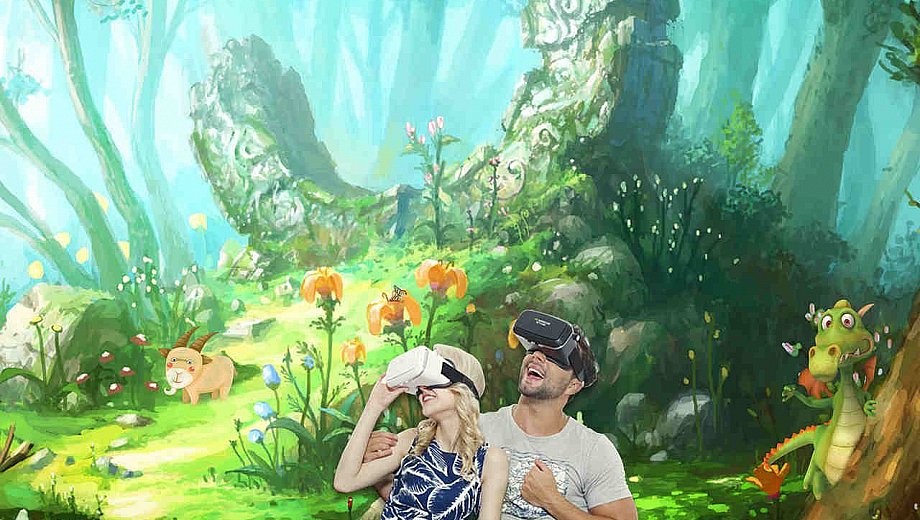 Zwei Menschen haben VR-Brillen auf uns gucken erstaunt um sich, wo sie einen verwunschenen Wald aus einer Fantasiewelt sehen.