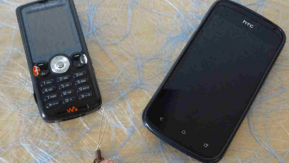 Auf einem Tisch liegt ein altmodisches Handy neben einem modernen Smartphone.