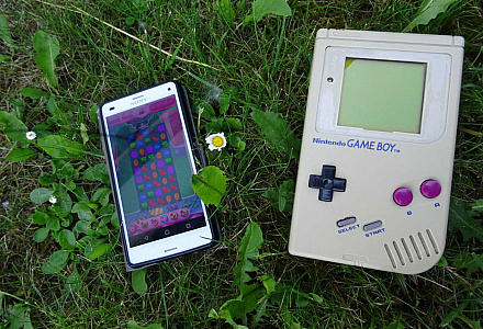 Ein Gameboy und ein Smartphone liegen nebeneinander im Gras.