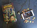 Auf einem Tisch liegt ein Harry Potter Roman, daneben eine Uhr, ein bisschen Kleingeld und ein Smartphone mit dem Mobile Game Hogwarts Mystery.