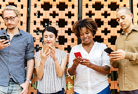 Vier Menschen stehen an einer Wand und gucken alle in ihr Smartphone.
