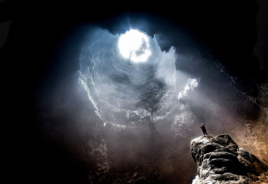 Mensch steht in einer großen Höhle mit einem Loch in der Decke