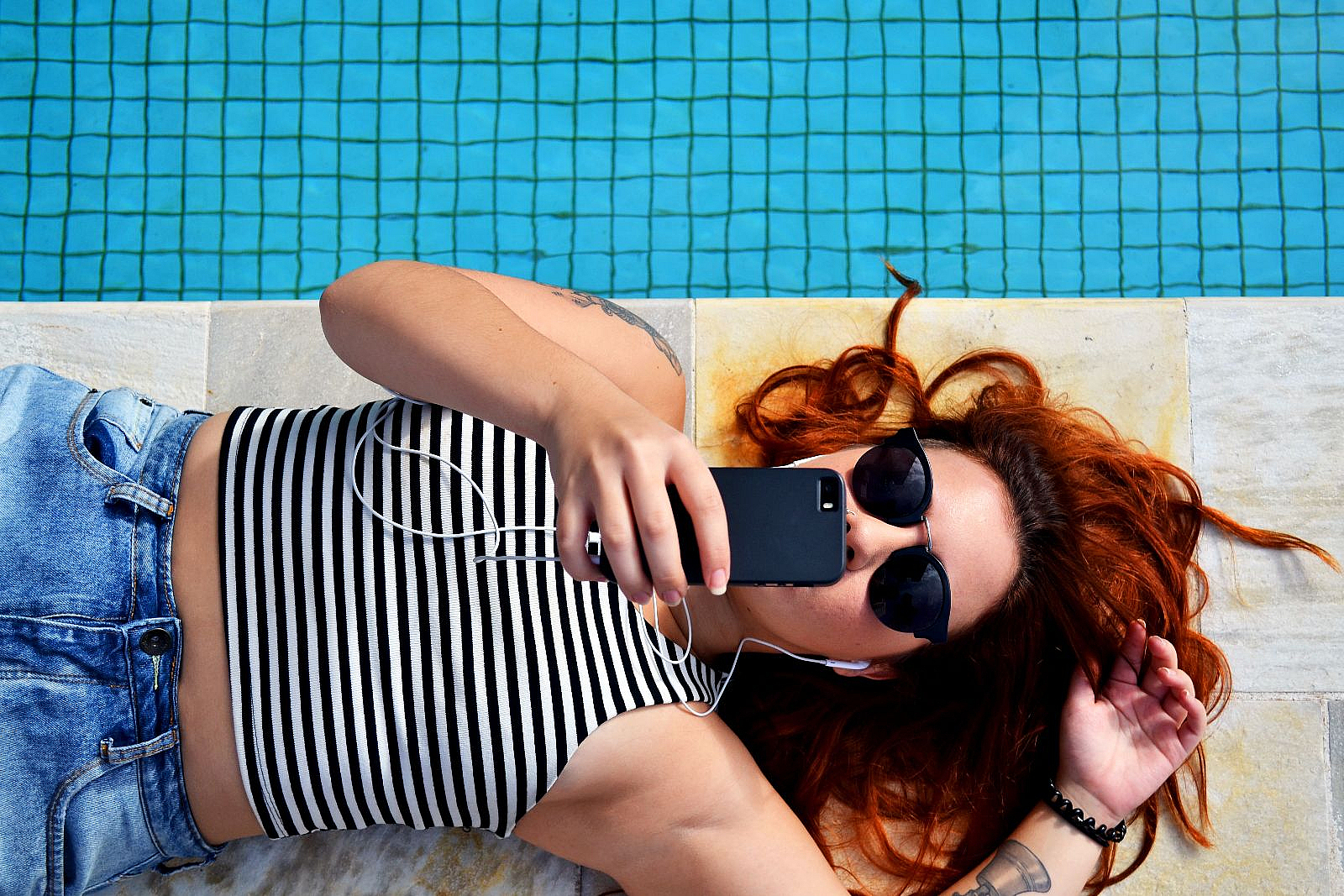 Frau liegt im Urlaub am Pool und hat ihr Smartphone in der Hand.