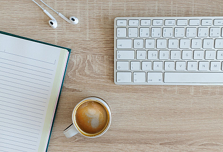 Schreibtisch mit einer Tastatur, einem Notizbuch und einer Tasse Kaffee
