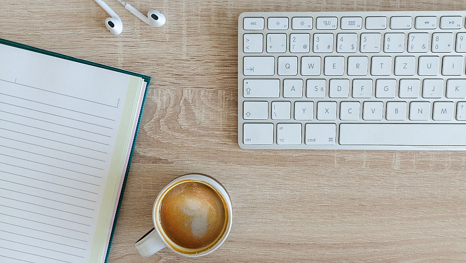 Schreibtisch mit einer Tastatur, einem Notizbuch und einer Tasse Kaffee