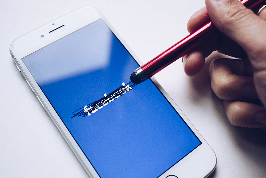 Ein Smartphone zeigt einen blauen Bildschirm mit Facebook-Logo. Mit einem Touch-Stift wurde das Logo durchgestrichen.