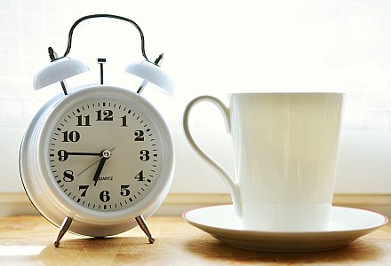 Ein Wecker und eine Tasse stehen auf einem Nachttisch. Das Handy bleibt bei der medienfreien Morgenroutine beiseite.