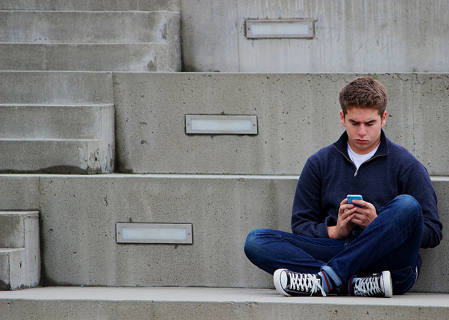 Junge sitzt alleine auf einer Treppe und guckt aufs Smartphone