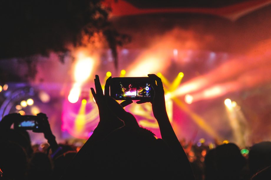 Auf einem Konzert wird ein Smartphone hochgehalten, um Fotos und Videos zu machen. 