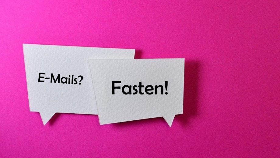 Pinker Hintergrund, davor zwei Sprechblasen. Die erste fragt: "E-Mails?". Die zweite antwortet: "Fasten!"