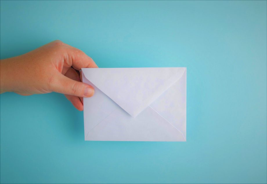 Hellblauer Hintergrund. Von links kommt eine Hand ins Bild, die einen leeren Briefumschlag hält. 