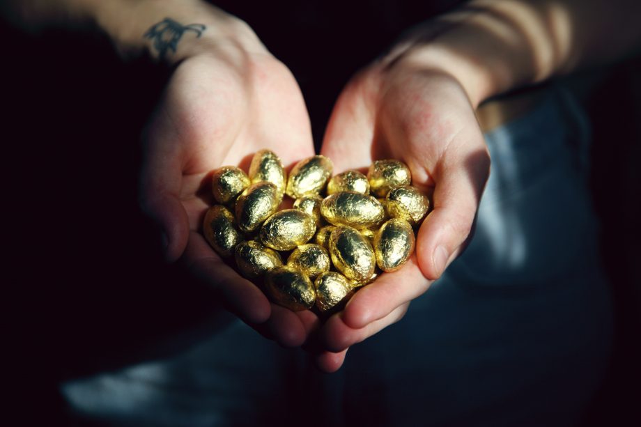 Zwei Hände halten ein Dutzend goldene Schokoladen-Eier. 