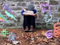 Person sitz alleine an einer Mauer und vergräbt das Gesicht in den Armen. Um sie herum Blitze und Wirbel wie aus einem Comic.