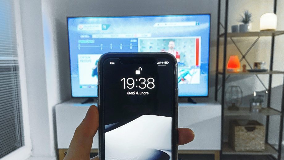 Blick aufs Handy, im hintergrund läuft der Fernseher