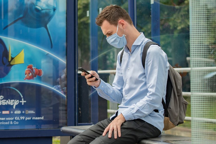 Mann mit Handy und Maske an Bushaltestelle