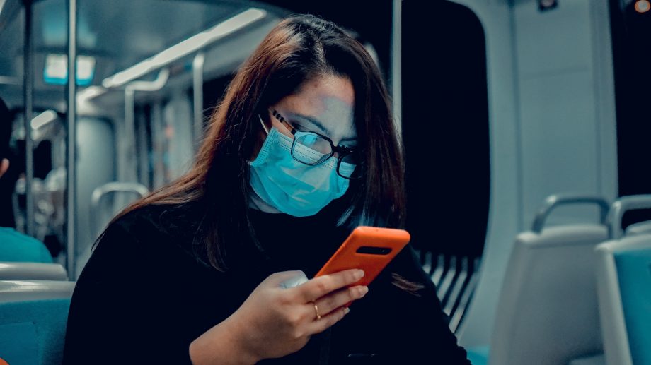 Frau mit Handy und Maske in U-Bahn