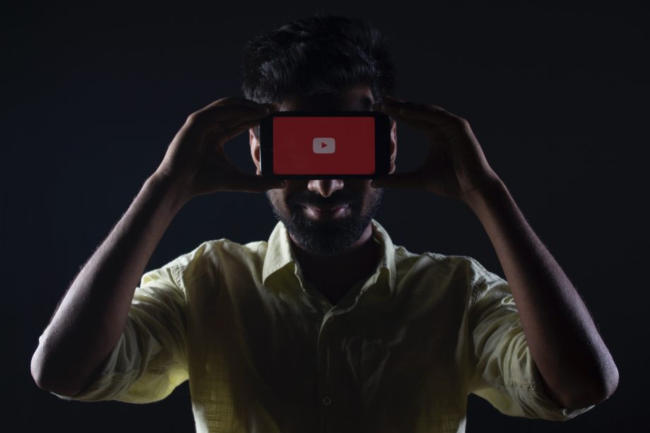 Mann hält Smartphone mit YouTube-Logo vor sein Gesicht