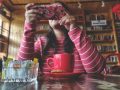 Frau am, Tisch, vor ihr ein Kaffee, hält das Smartphone vors Gesicht