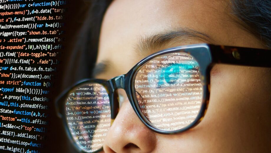 In der Brille einer Frau spiegelt sich Programmiercode