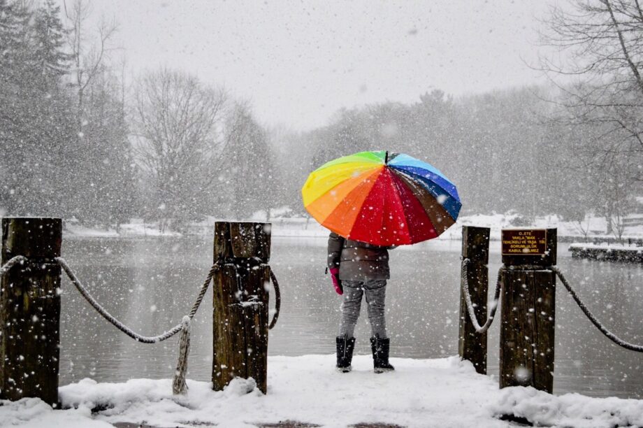 Mensch mit buntem Regenschirm steht im Schnee